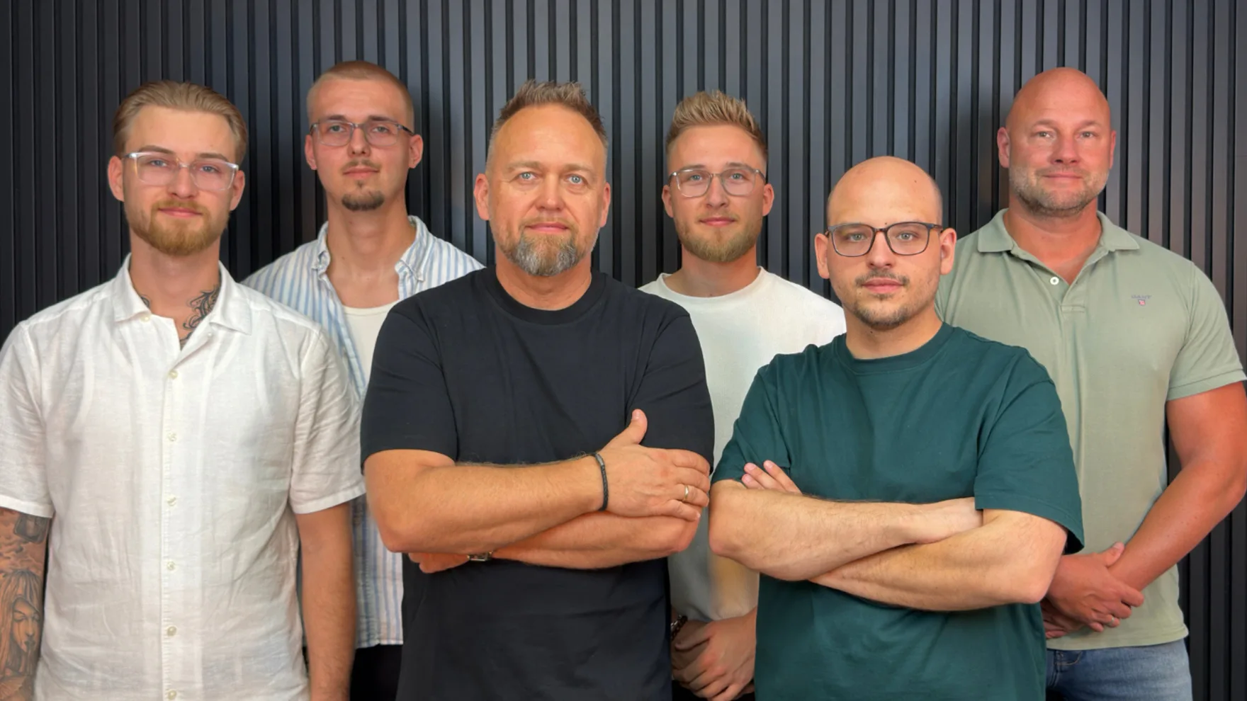 Das sechsköpfige Team von PLAN 4 LIFE steht gemeinsam vor einer dunklen Lamellenwand.