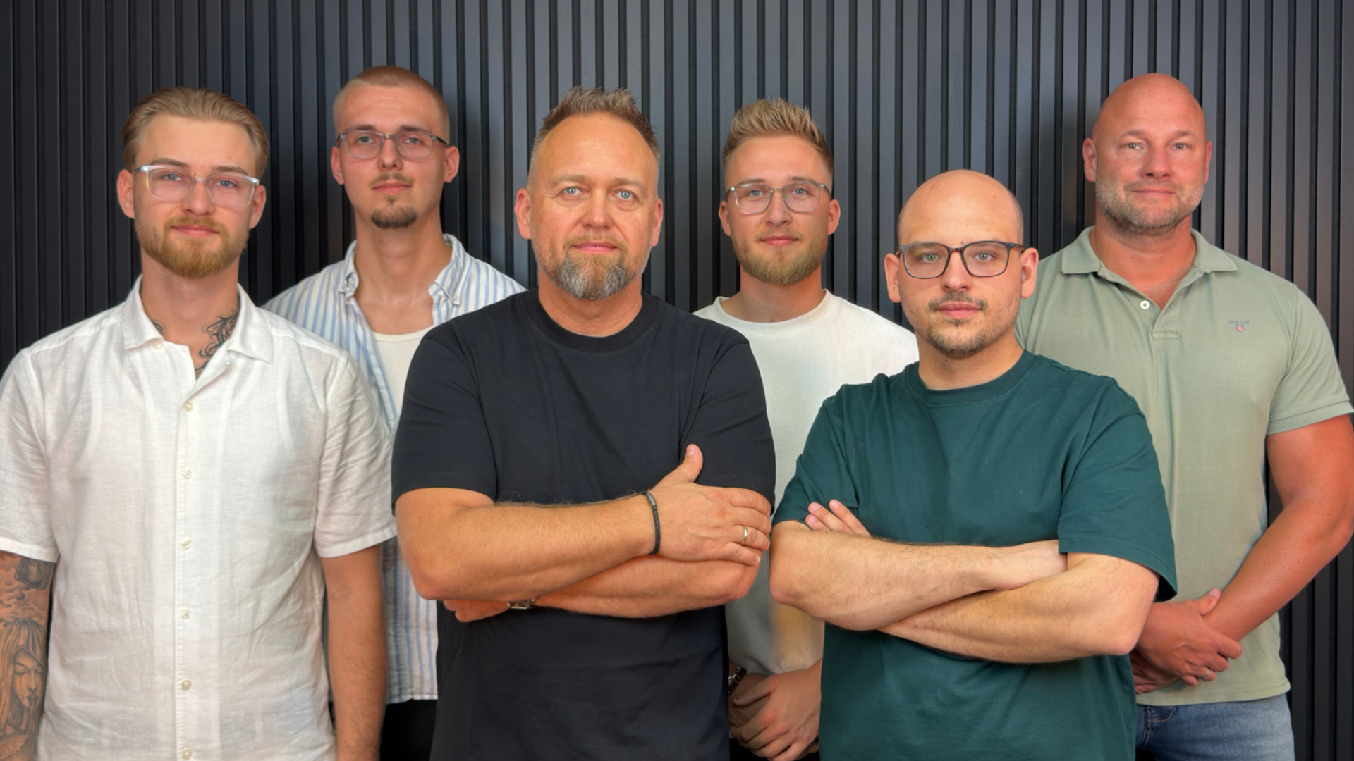Das sechsköpfige Team von PLAN 4 LIFE steht gemeinsam vor einer dunklen Lamellenwand.